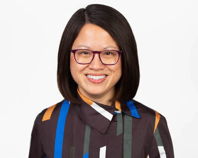 Asian woman with shoulder-length black hair wearing purple glasses and a graphic print silk shirt