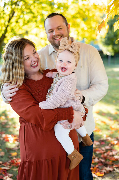 Happy parents looking at their 1 year old baby who is smiling in fall family photos