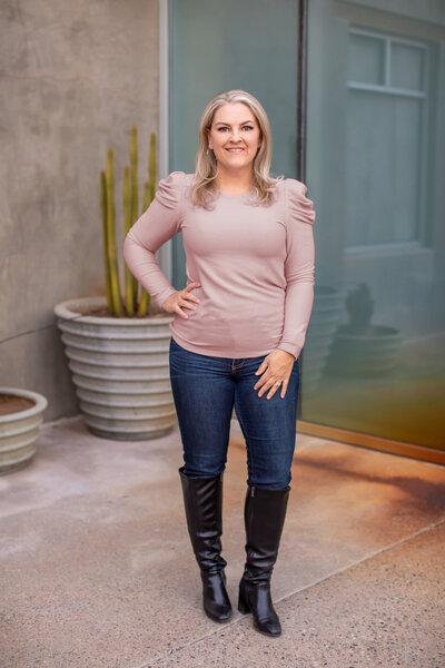 A wedding photographer's headshot image. She's wearing a pink sweater posing in front of the camera.
