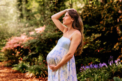 Mom to be holds her pregnant bump while walking and looking back at dad in a field at sunset. 