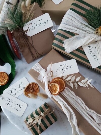 Christmas gifts wrapped in kraft paper with calligraphy gift tags, pine and dried oranges