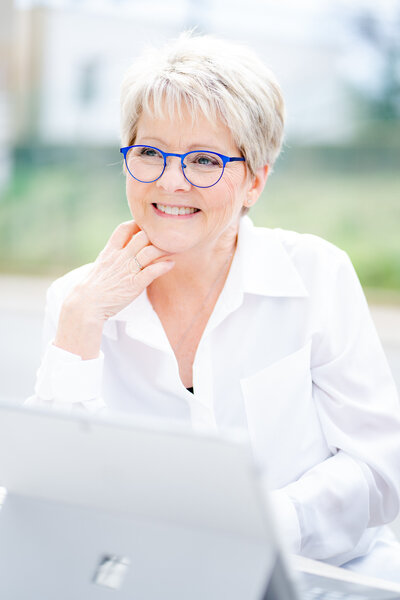 Creative business owner smiles up over the back of her computer, showing off her blue glasses