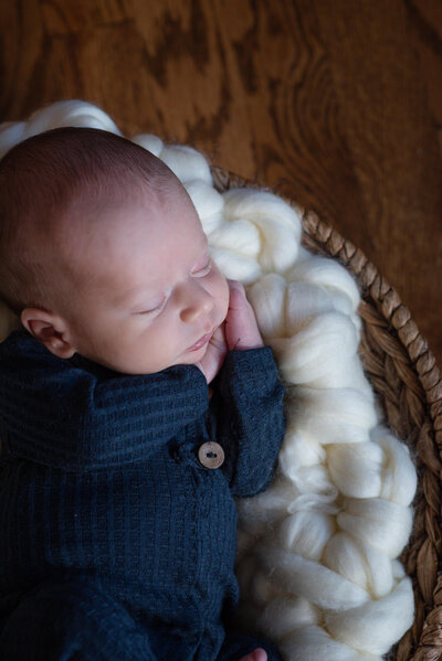 An image of a newborn baby sleeping in a blue onesie in a woven basket