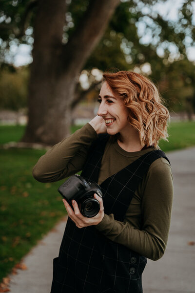 girl holds camera smiling on concrete path