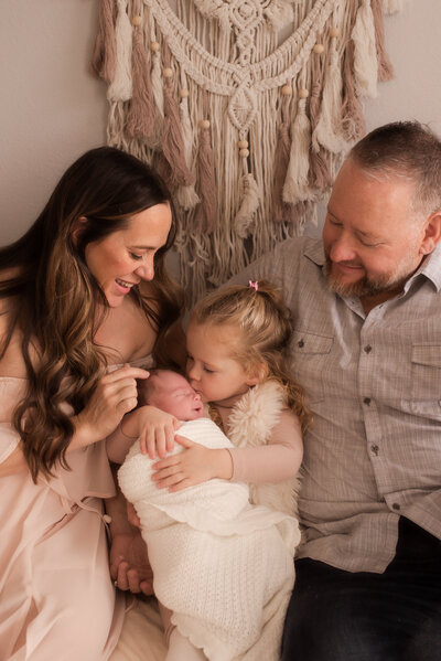 A new family of four sitting and loving on their newborn baby.