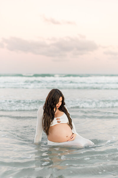 An Orlando photographer captures a beautiful pregnant mother kneeling in the water holding her belly