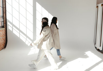 two women walking in different directions passing each other in front of white backdrop