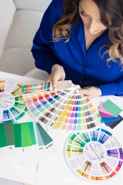 Color psychology expert in royal blue blazer reviewing professional Pantone color fans and swatches during strategic brand development session