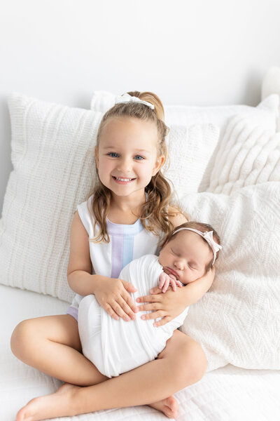 Smiling big sister holding baby on the bed in the studio