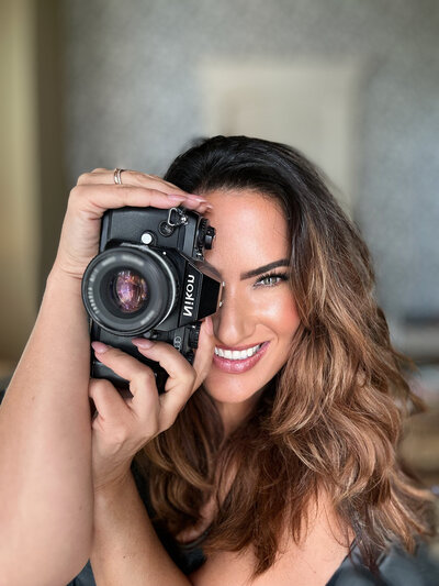 Chelsea, a luxury wedding photographer in San Antonio, smiling and holding a camera, passionate about capturing love stories.