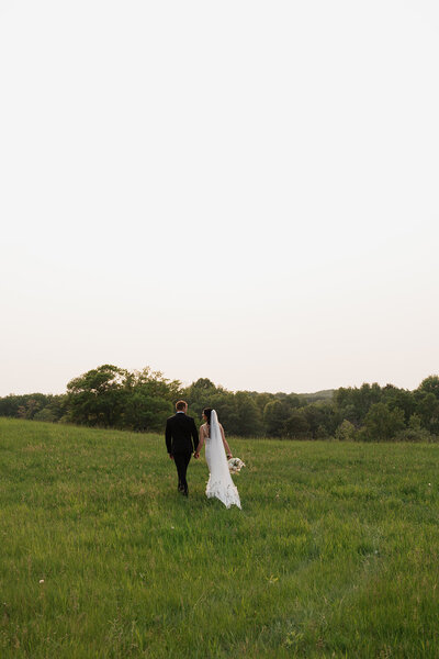 Bride and groom walking hand in hand through a scenic field in Duluth, Minnesota during their wedding photoshoot