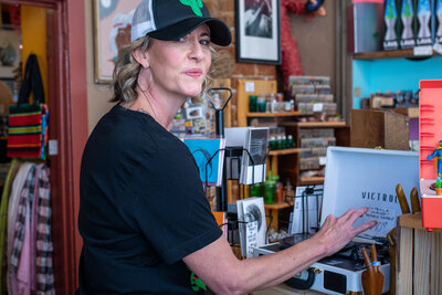 Woman in a black shirt and hat working inside a colorful retail shop, adjusting a record player, photographed by Vyrl Photo for business photography Tucson.