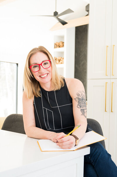 A woman with glasses and a tattoo sits at a desk, focused on her work with a thoughtful expression.