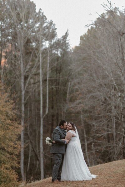 A bride and groom hugging and kissing with fall colors in the background