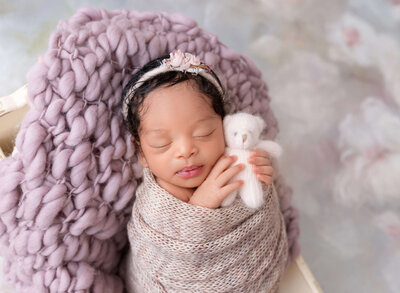 Rochel Konik Photography | Top NYC Brooklyn Newborn Photographer captures baby girl wrapped in white tulle with pearl embellishments. Baby's hands are peeking out of the wrap and resting under baby's chin. Baby is sleeping and wearing a white headband.