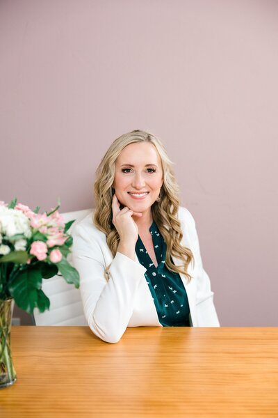Two women posing for a headshot; one is sitting while the other stands beside her, both looking at the camera.