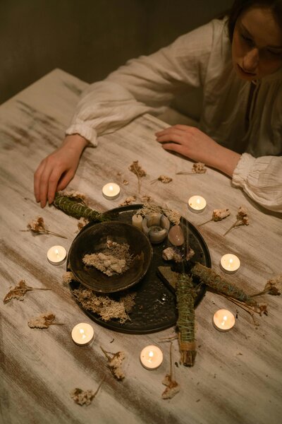 Overhead view of a wooden table with lit candles, herbs, and ceremonial objects arranged for a ritual.