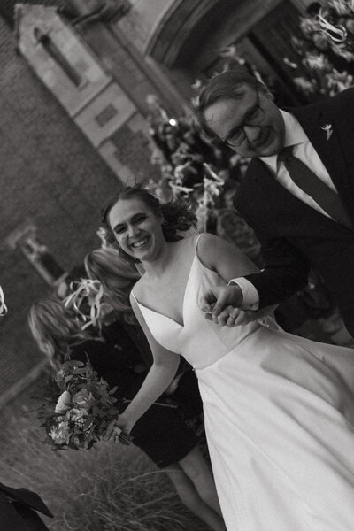 Newlyweds hold hands and run out of the church together, surrounded by streamers and loved ones