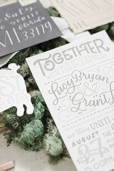 Close-up of a playful wedding invitation sitting on a bed of moss, letterpress printed in two tones of grey ink