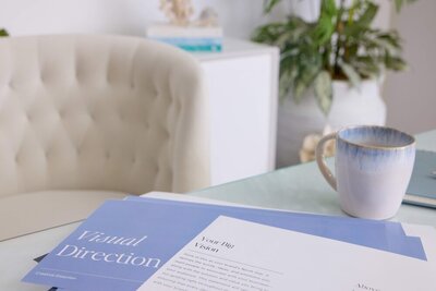 Flat lay of a Visual Direction brand document with a coffee cup and tufted chair—showcasing the creative and strategic process at Jennifer Taormina & Co.