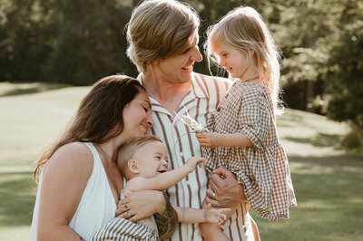 Emotive lifestyle session in Charlotte—family of four cuddles close, admiring a bloom.