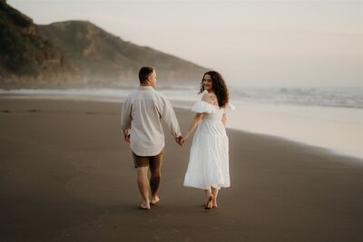 A couple walking along a black sand beach during an engagement photoshoot with Tashina Narelle, An Auckland, Waikato and Bay of Plenty Wedding and Portrait Photographer