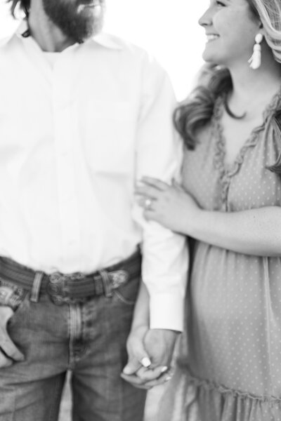 black and white photo of a couple holding hands with a cowboy belt, white shirt, up close picture