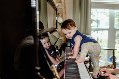 A baby girl climbing on the piano