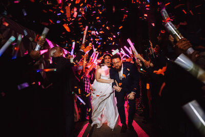 A bride and groom make their wedding exit running through a colorful crowd of their guests