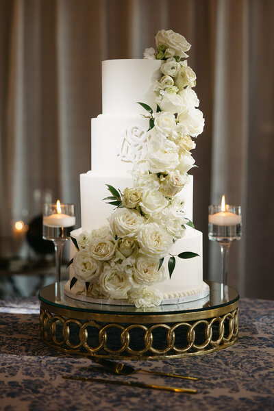 Elegant white wedding cake with cascading roses on a gold stand, a refined touch from The Eventful Gals, luxury wedding planners in Northeast Florida.