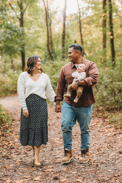 Toddler brother sits with his little sister as mom and dad look adoringly in the background during harrisburg family photos