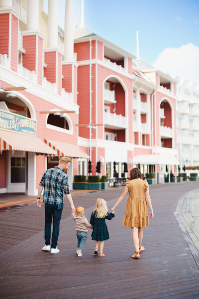A photo of a family of four walking along the boardwalk with pink buildings in the background.