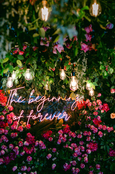 neon sign on pink florals that reads, "the beginning of forever"