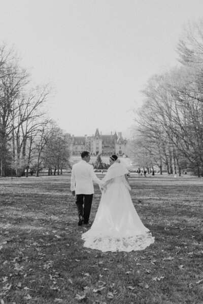 Romantic wedding couple in their bridal attire walks down in front of the Biltmore Estate.