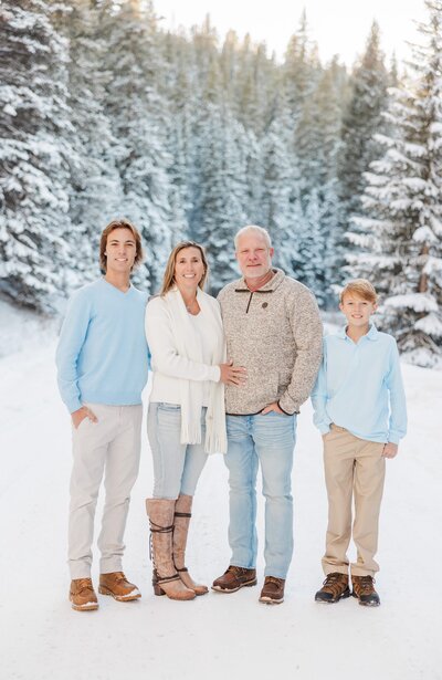A mom and dad stand in a snow covered mountain in blue and white smiling for their Breckenridge Family Photographer