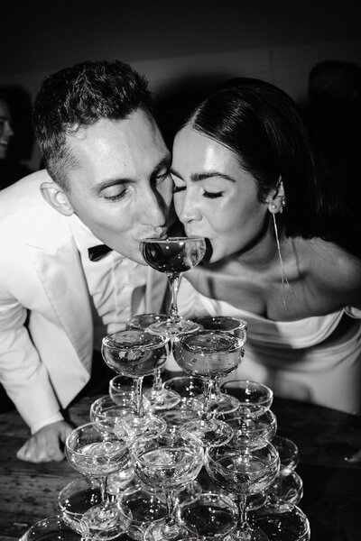 Candid photography of bride and groom sipping from champagne tower