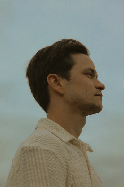 A portrait of a man. It is from his side profile as he looks away.