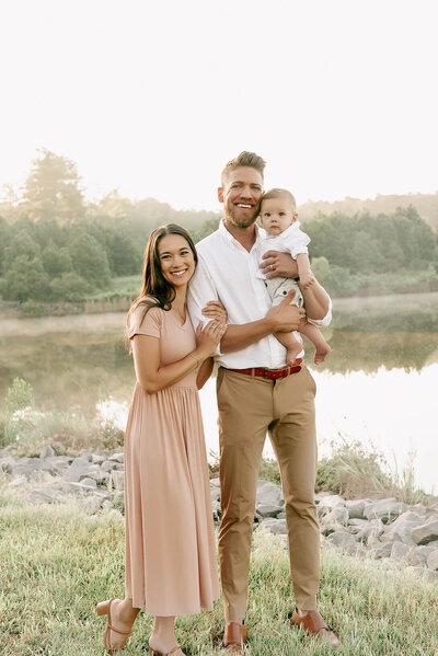 a family of three by a lake posing for a photo by rosa ashdown