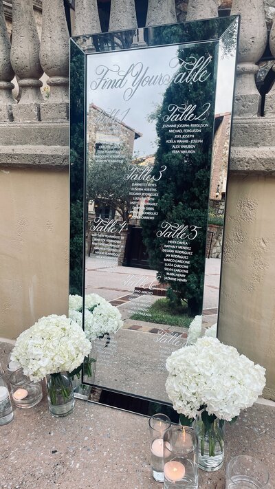 Black wedding mirror with white calligraphy flanked by white hydrangea arrangements