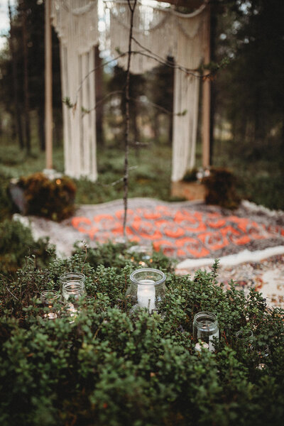 Candles and beautiful rugs adorn the forest floor in a lovely forest summertime wedding ceremony in the Swedish Arctic.