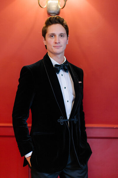 groom standing in front of red wall