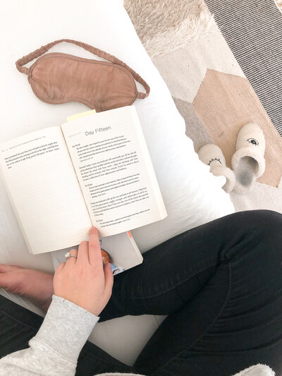 Image from above of crossed legs on a couch with an open book sitting next to an eye mask