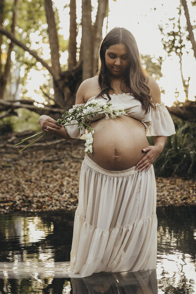 Pregnant mother rubbing her baby belly, with flowers in a creek at Mt Tamborine