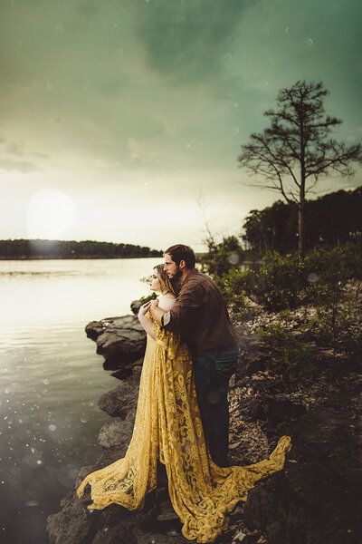 man embraces woman during engagement session at the lake
