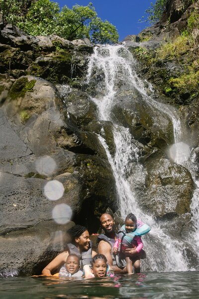 A family in the water with a waterfall behind.
