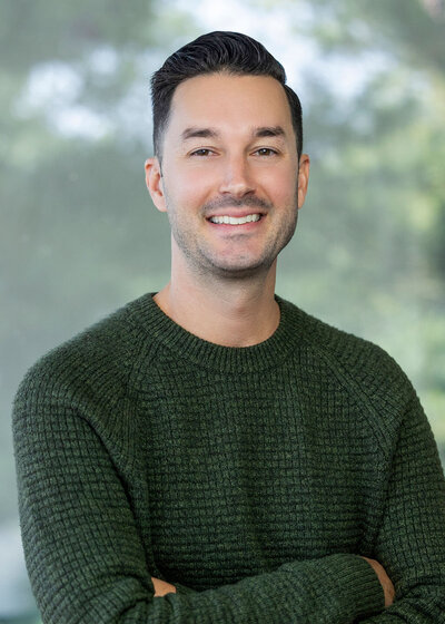 Man in a green sweater with short dark hair smiling against a green background