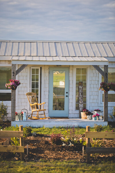 white cottage with blue door and rocking chair on porch