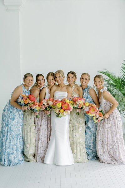 Bride standing with bridesmaids holding colorful bouquets.