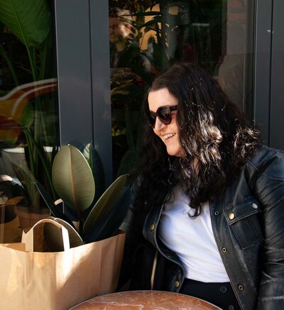 Martina Menzini sitting at outdoor cafe table surrounded by lush greenery.