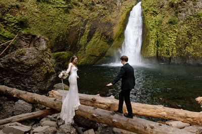 Elopement couple balancing on a log in front of a waterfall at the Columbia River Gorge.